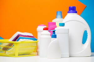 Photo of bottles of cleaning products and multi-colored towels in basket isolated on blue, orange background